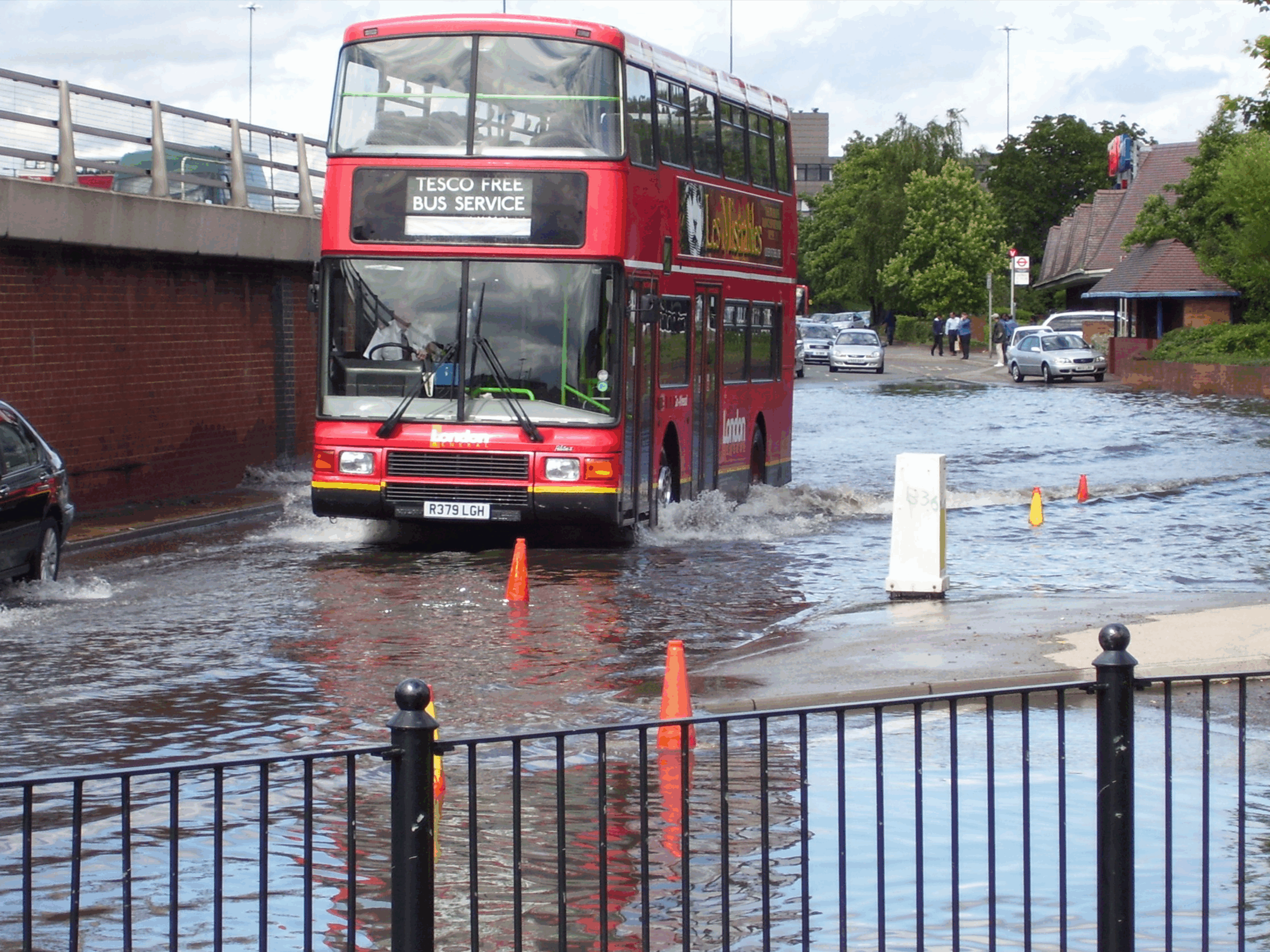 A red double-decker bus navigates through floodwaters