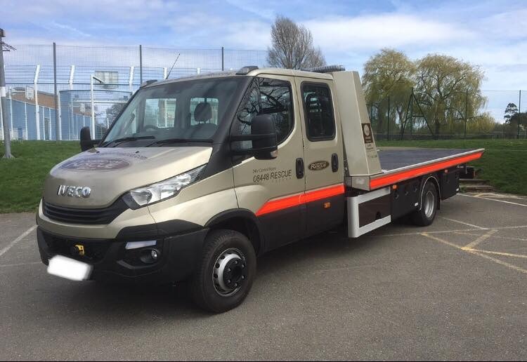 Iveco rescue vehicle parked on asphalt, showcasing a flatbed design and marked with contact information for emergency services.